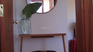 Una stanza con una porta in legno, un tavolino con una bottiglia di vetro e una foglia, e uno specchio sul muro.