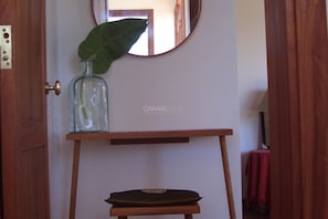 Une pièce avec une porte en bois, une petite table sur laquelle se trouvent une bouteille en verre et une feuille, et un miroir accroché au mur.