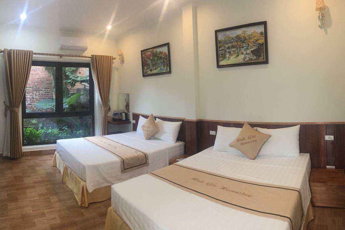 A hotel room with two beds, a window with curtains, a brick wall outside, and two framed pictures on the wall.