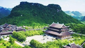Ein traditioneller chinesischer Gebäudekomplex mit mehreren pagodenartigen Bauwerken, umgeben von üppiger Vegetation und einem markanten Berg im Hintergrund.