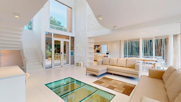 A spacious living area with a glass coffee table, a sofa, and a dining area with a table and chairs.
