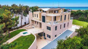 A multi-story building with a pool, surrounded by greenery and a view of the sea.