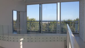A modern interior with large windows offering a view of trees and a beach.