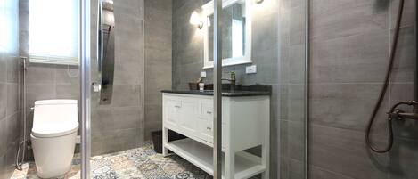 A modern bathroom with a glass shower enclosure, a white vanity with a mirror, and patterned floor tiles.