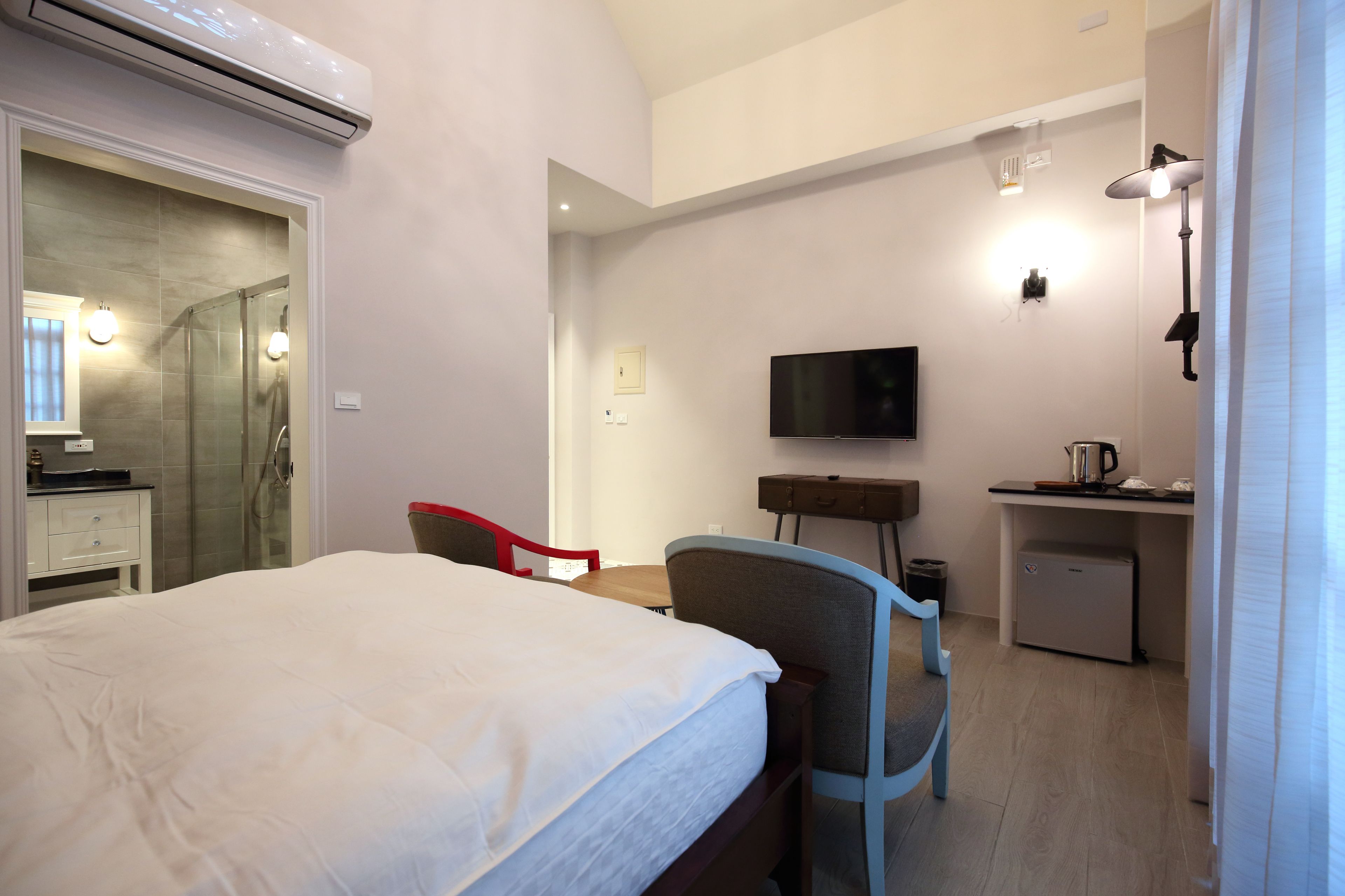A hotel room with a bed, a desk, a chair, a television, and a shower area.