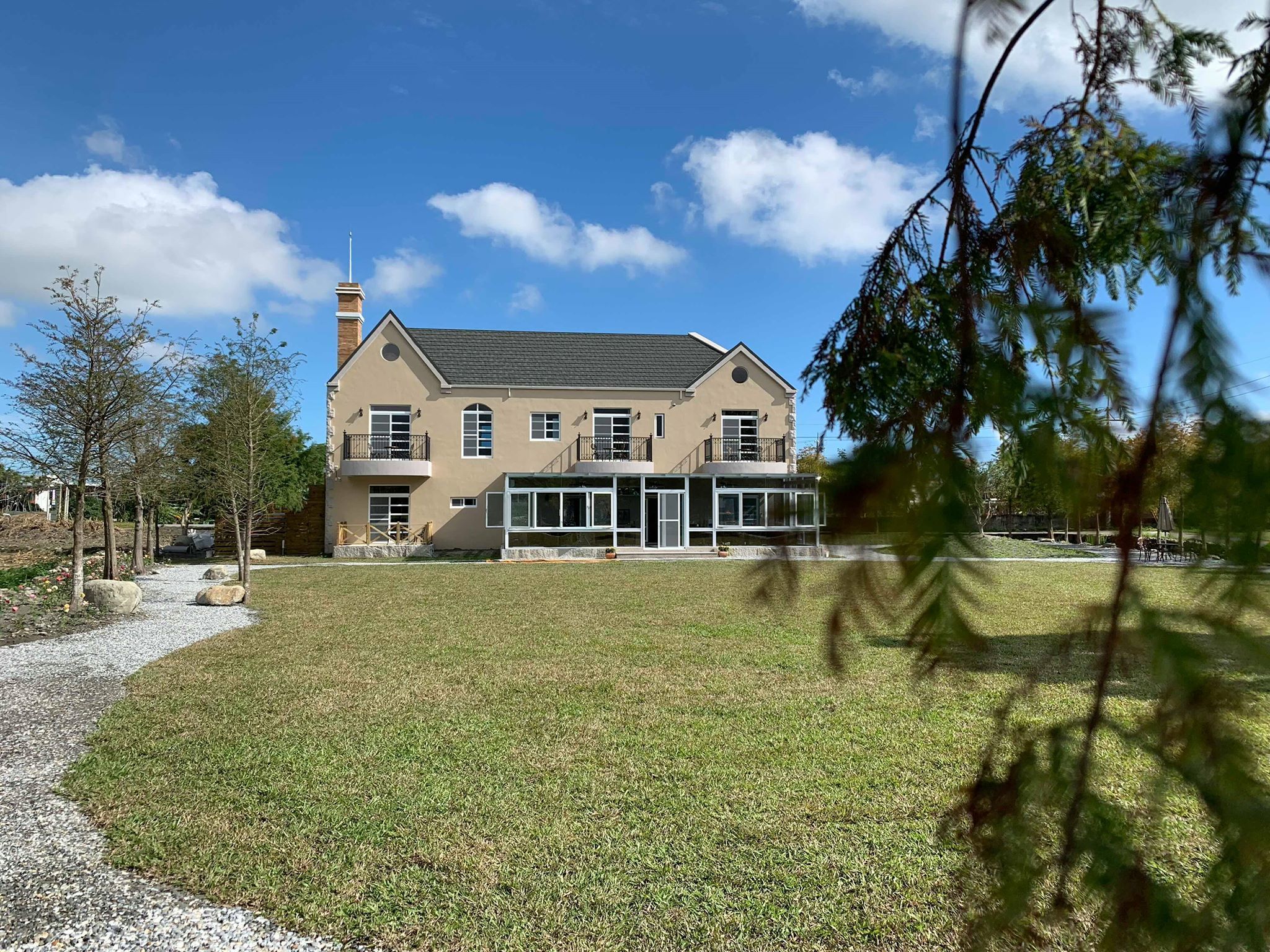 A two-story house with a large front lawn, a visible chimney, and a balcony on the upper floor.