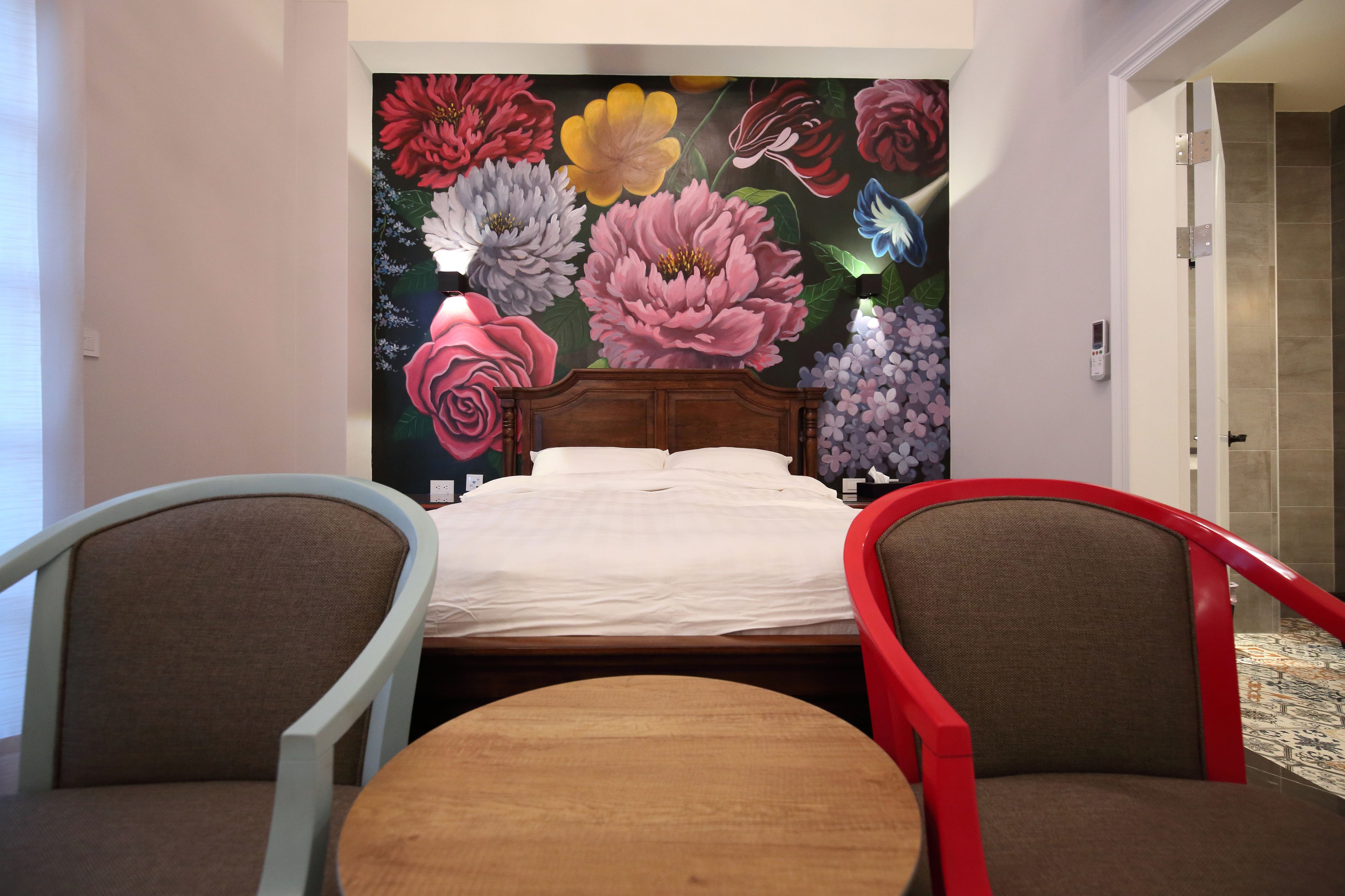 A bedroom with a large floral mural on the wall, a wooden bed, two chairs, and a small round table.