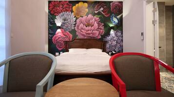 A bedroom with a large floral mural on the wall, a wooden bed, two chairs, and a small round table.