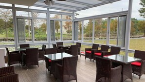 A spacious indoor area with large windows, wicker furniture, and a glass table. - Serrado Manor (Ji'an)