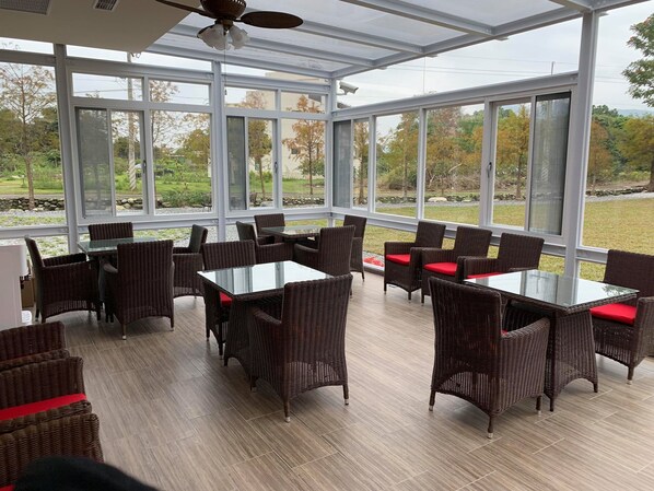 A spacious indoor area with large windows, wicker furniture, and a glass table. - Serrado Manor (Ji'an)