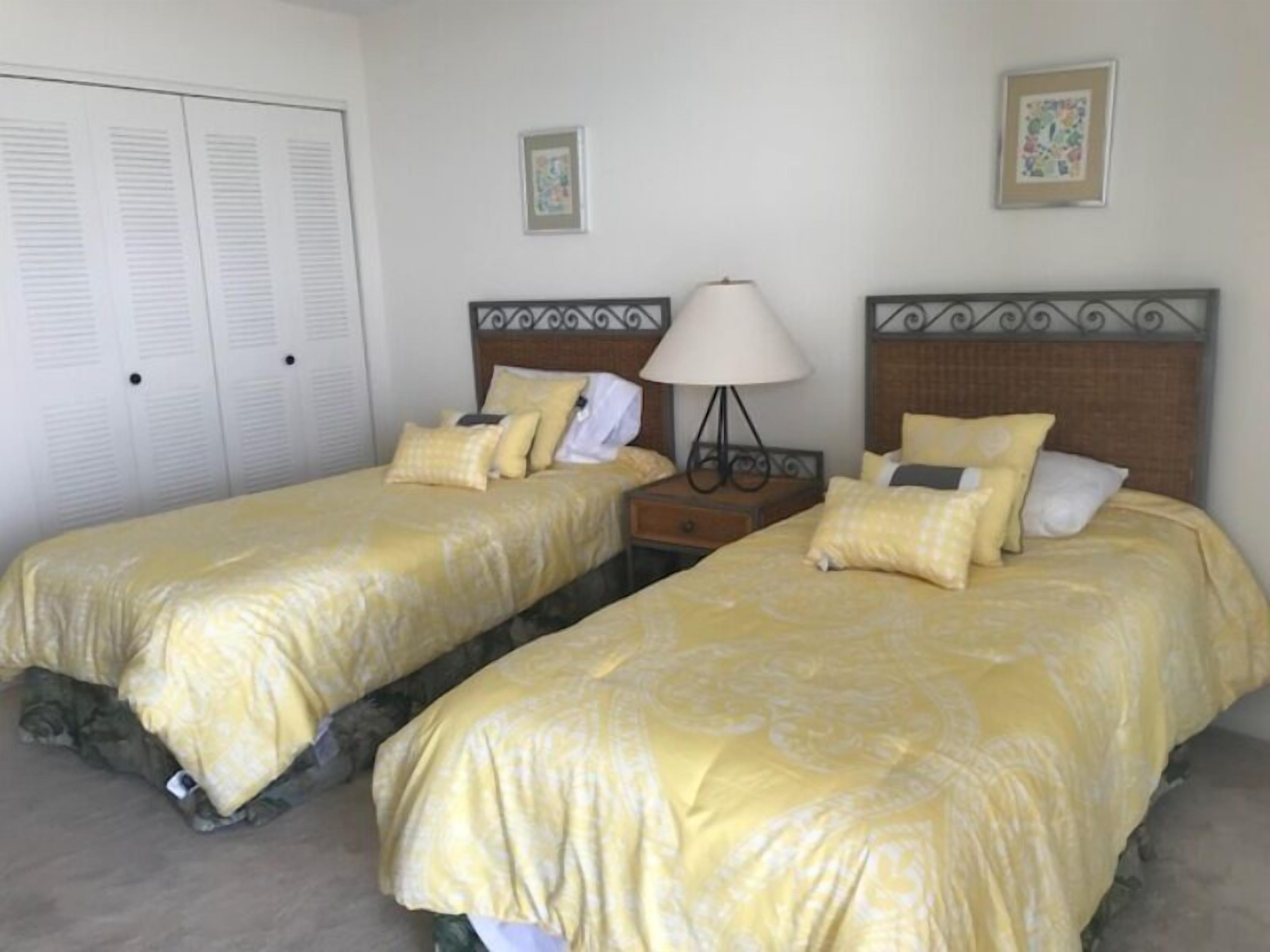 A bedroom with two beds, a nightstand, a lamp, and a closet.