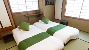A traditional Japanese-style room with tatami flooring, two beds with green and white bedding, a small shelf with decorative items, and a window with a view. - KAGURAZAKA RETRO BAR & HOTEL (Tokyo)
