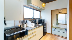 A modern kitchen with a stove, microwave, and sink. There is a window providing natural light, and a sliding door leading to a tatami mat room. - KAGURAZAKA RETRO BAR & HOTEL (Tokyo)