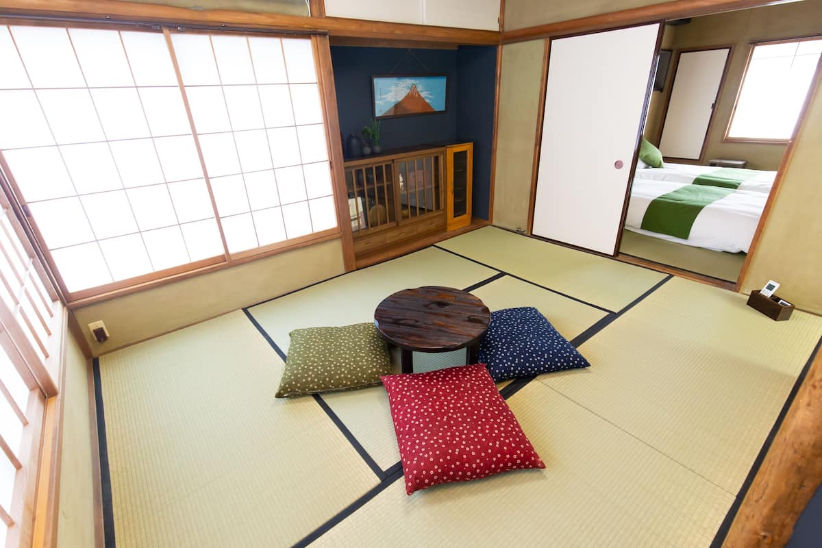 Een kamer met tatami matten, een tatami tafel, kussens, een klein kastje en een schilderij aan de muur.
