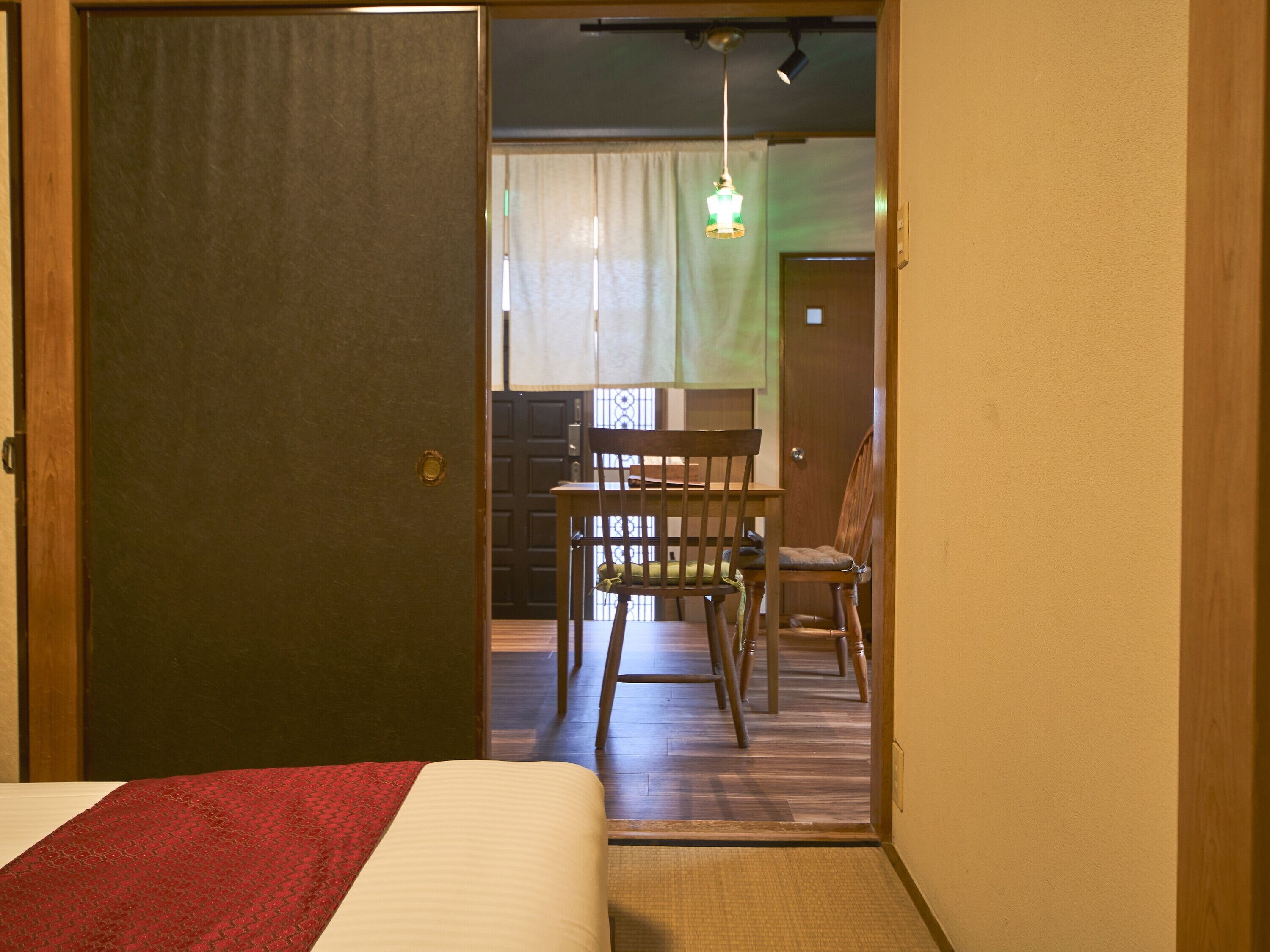 A hotel room with a bed, a wooden door, a dining table with chairs, and a hanging light fixture.