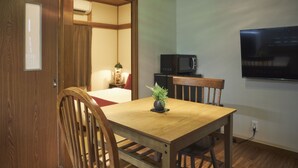 A wooden dining table with chairs, a small potted plant, a microwave, and a TV mounted on the wall. - KAGURAZAKA RETRO BAR & HOTEL (Tokyo)
