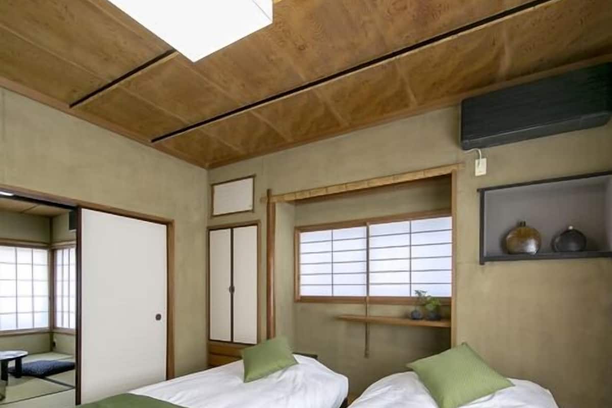 Een kamer met twee bedden, een raam, een plank met decoratieve objecten en een traditionele schuifdeur.