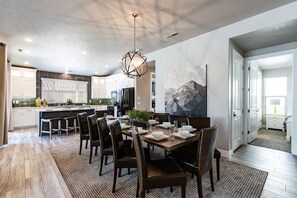 A modern kitchen with a dining area, featuring a large island, dark wooden chairs, and a contemporary chandelier.