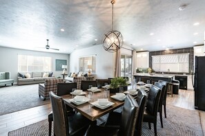 A modern kitchen with a dining area, featuring a central island, pendant lighting, and a view to the living room.