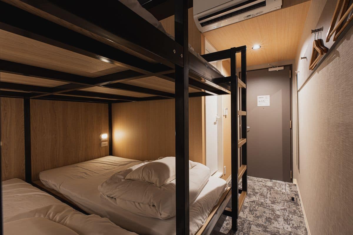 A compact, well-lit room with bunk beds, a wooden ceiling, and a small kitchenette area.