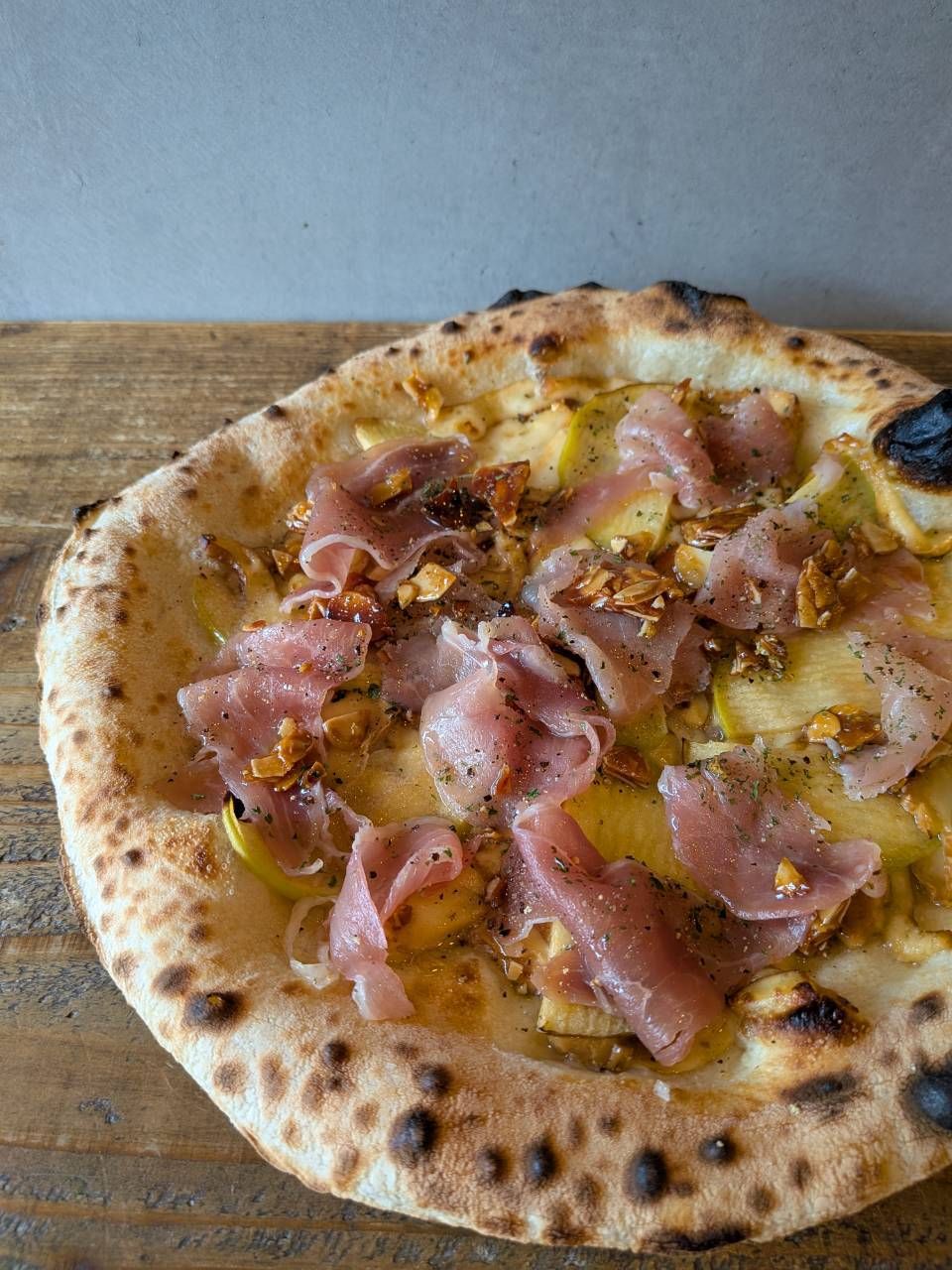 A pizza with ham and cheese on a wooden surface.