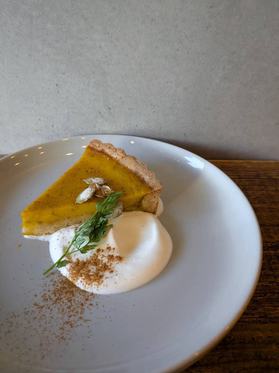 A slice of pumpkin pie on a white plate with a dollop of cream and a sprinkle of cinnamon.