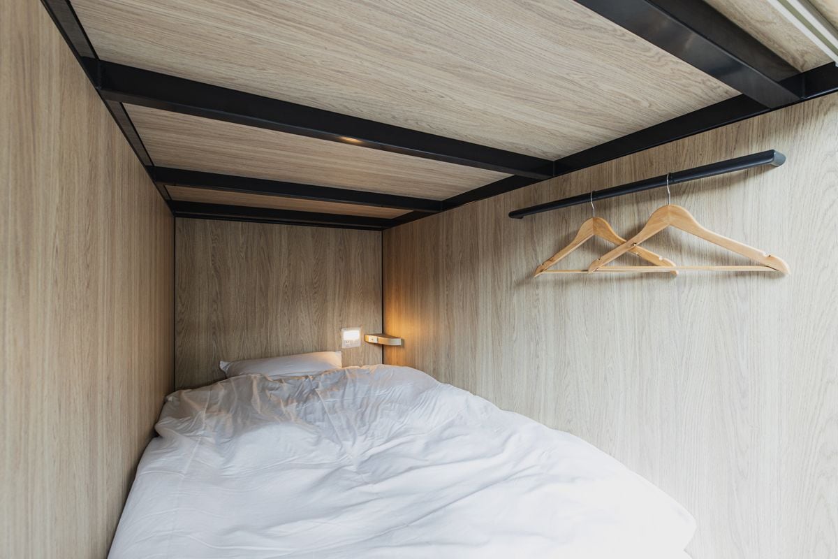 A bedroom with a bed, wooden walls, a black ceiling beam, and wooden hangers on a wall.