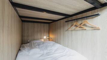 A bedroom with a bed, wooden walls, a black ceiling beam, and wooden hangers on a wall.