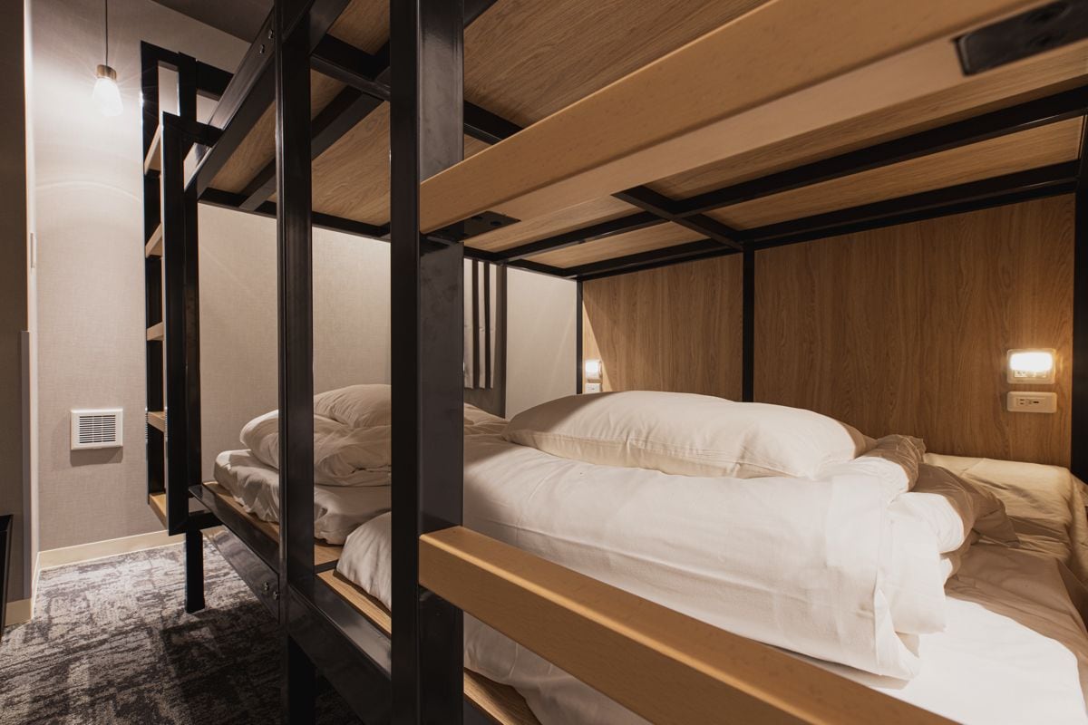 A bunk bed room with wooden beams, a light switch, and a wall-mounted light fixture.