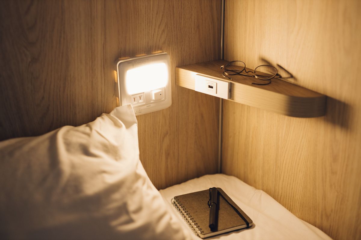 A bedside table with a lamp, a notepad, and glasses.