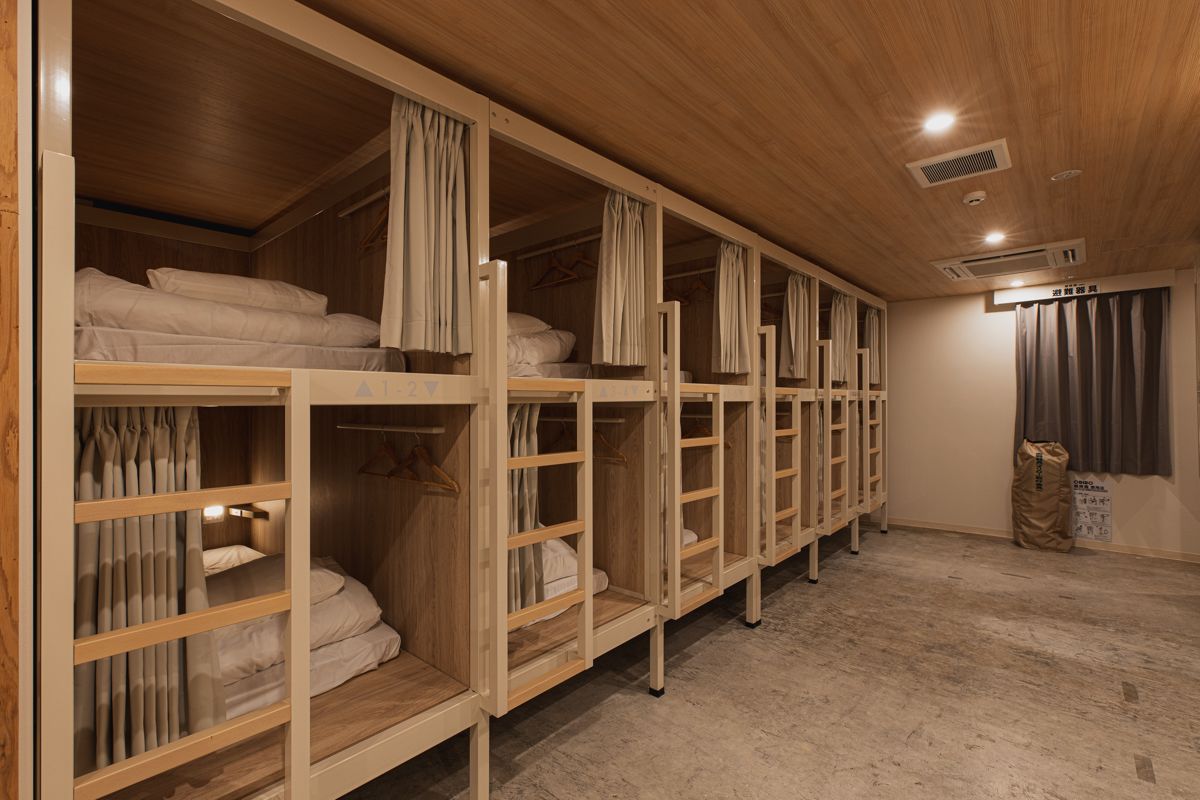 A row of bunk beds with curtains, wooden flooring, and a ceiling with recessed lighting.