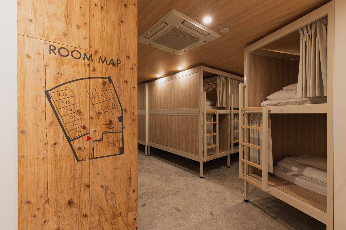 A room with bunk beds, a wooden wall with a room map, and an air conditioning unit.