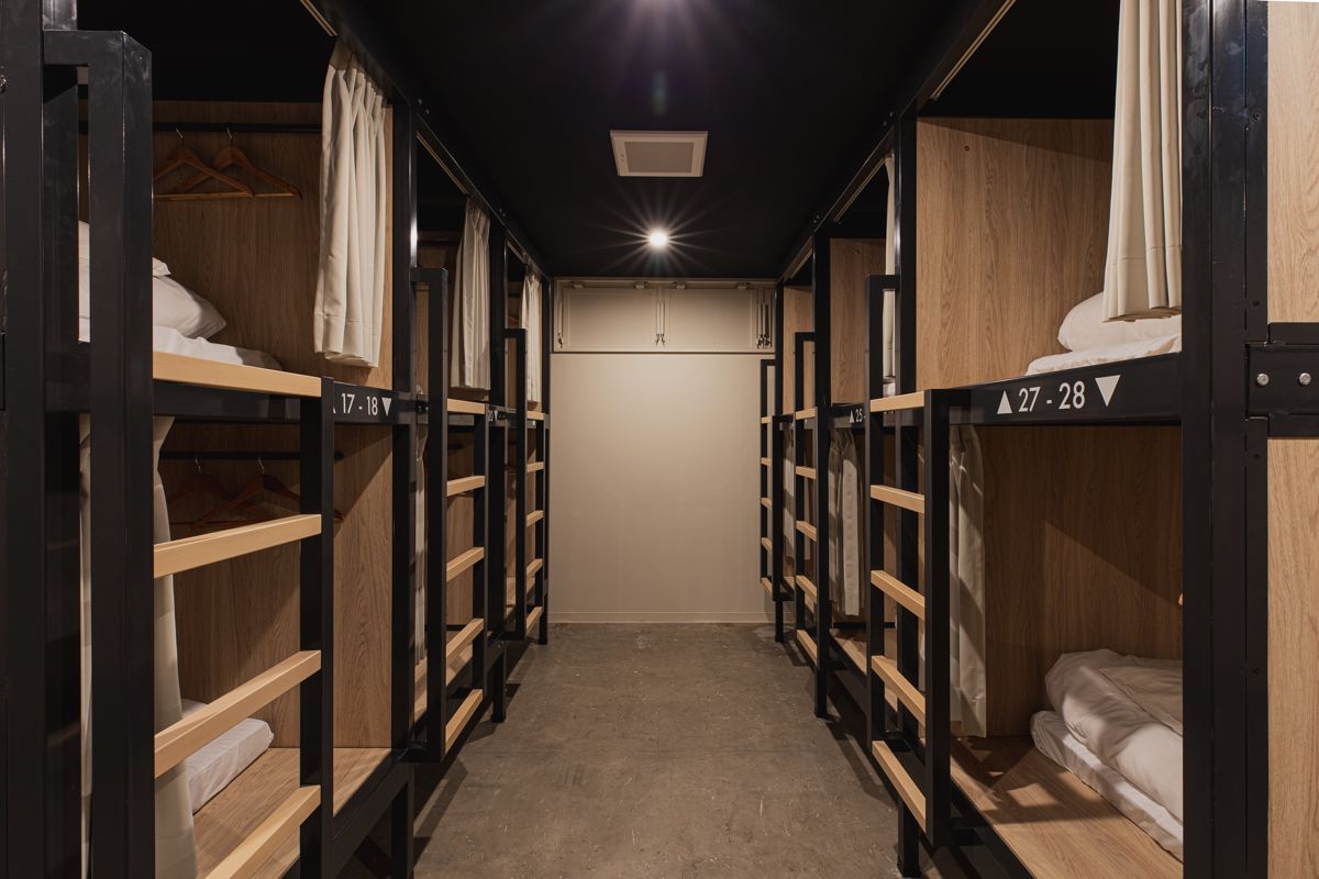 A corridor with bunk beds labeled 17-18 and 27-28, wooden walls, and a ceiling light.