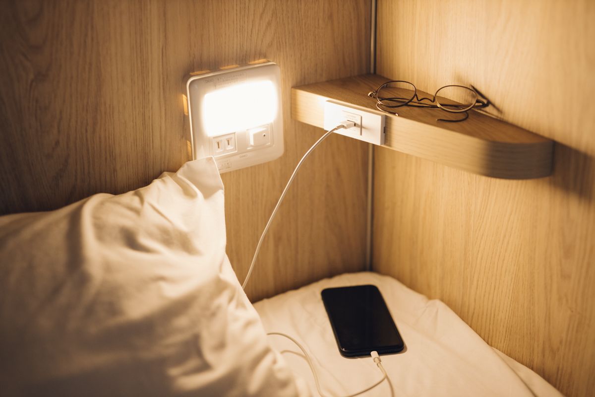 A bedside table with a smartphone and glasses, connected to a wall socket.
