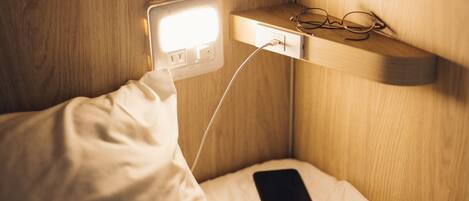A bedside table with a smartphone and glasses, connected to a wall socket.