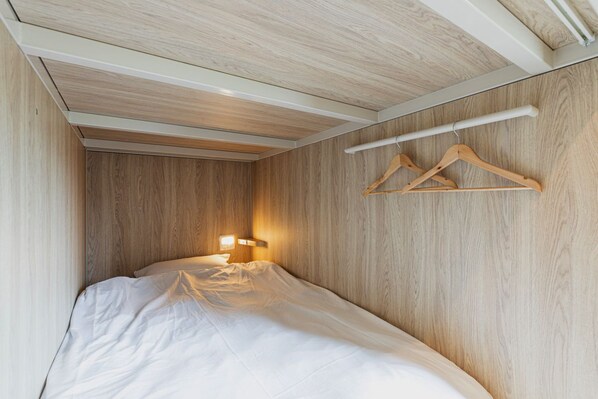 A bedroom with a wooden wall, a bed with white bedding, a bedside lamp, and wooden hangers on the wall. - Mash Café & Bed NAGANO - Hostel (Nagano)