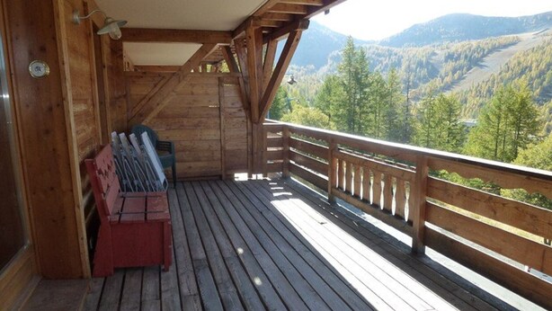 Terraza de madera con un banco y una caja roja, con vistas a un paisaje montañoso.