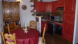 Una cocina compacta con armarios rojos, un microondas, un lavavajillas y una mesa de comedor con sillas.