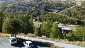 Un paisaje montañoso con una carretera, dos coches estacionados y un edificio a lo lejos.