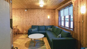 A cozy room with wooden walls, a green sofa, a round coffee table, and a window with a view. - Awesome home in Sysslebäck with WiFi (Sysslebäck)