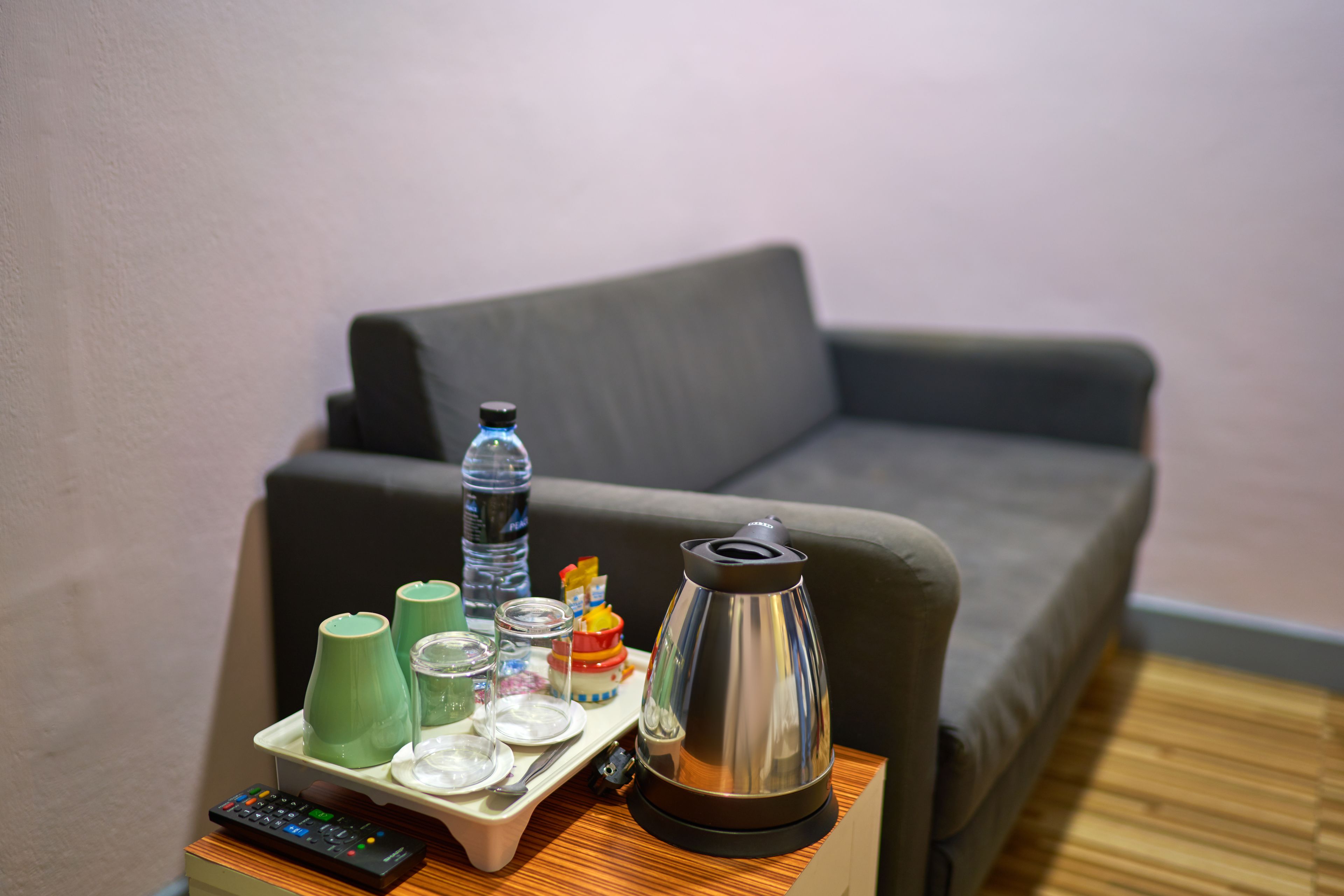 A room with a grey sofa, a tray with a kettle, glasses, and a water bottle.