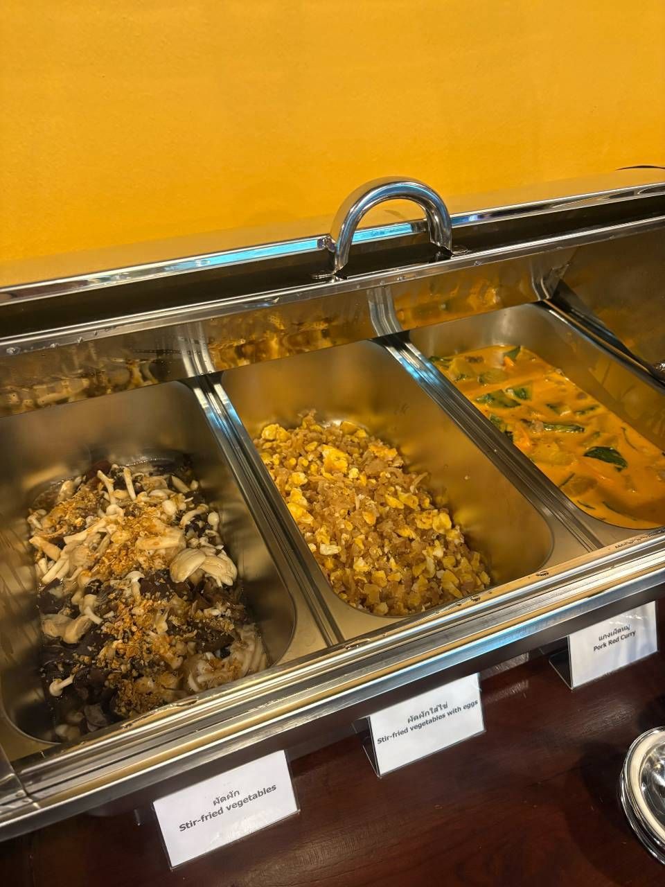 Un buffet proposant différents plats, chacun étant clairement identifié, notamment des légumes sautés et des œufs.