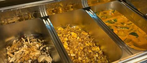 Un buffet proposant différents plats, chacun étant clairement identifié, notamment des légumes sautés et des œufs.