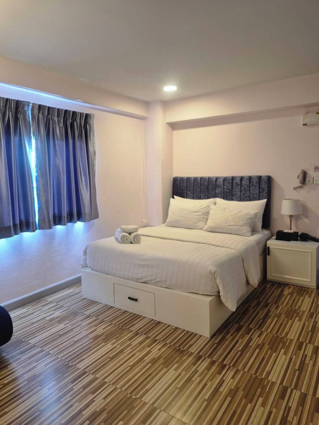A hotel room with a bed, bedside table, and a window with curtains.