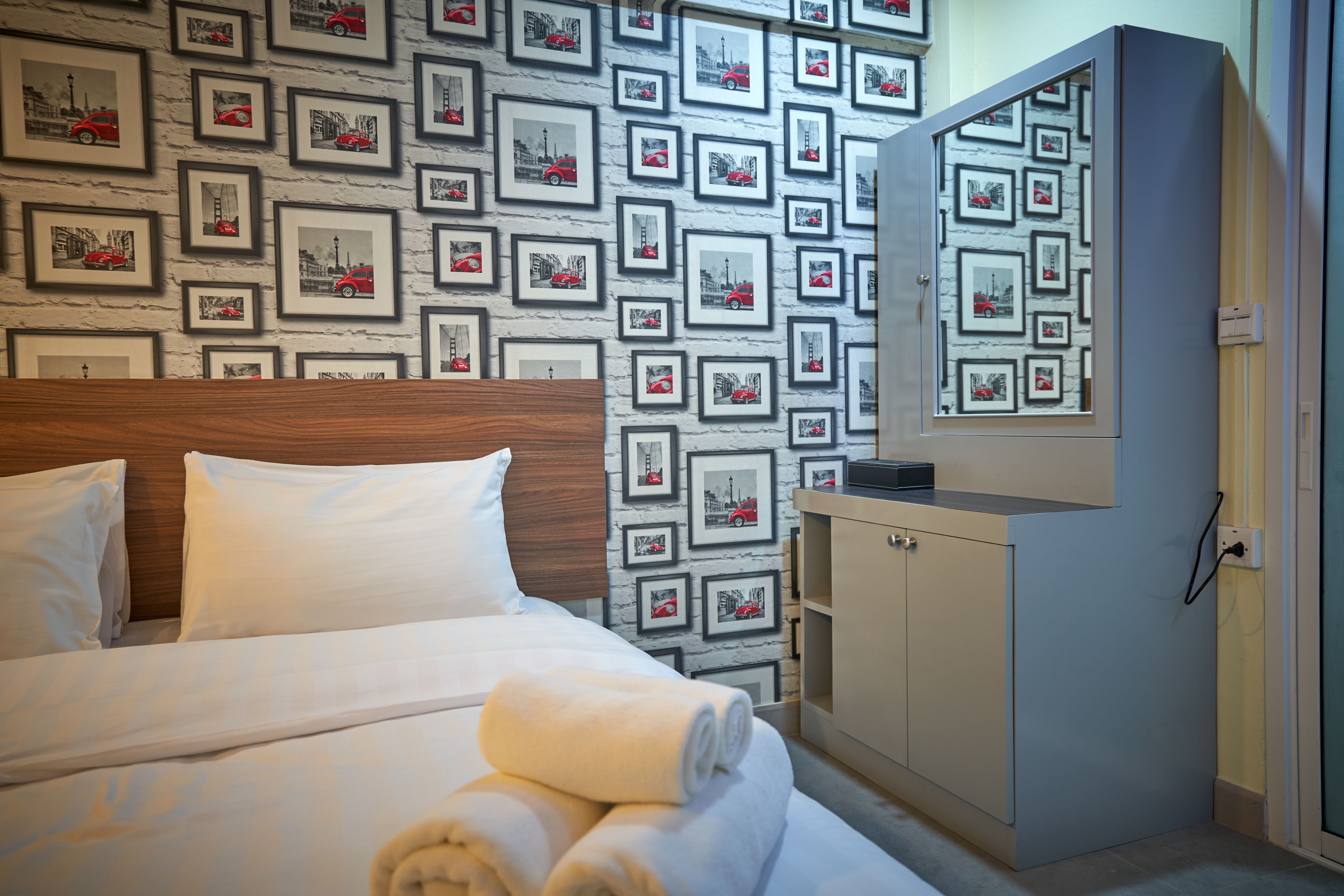 A hotel room with a bed, a wardrobe, and a wall decorated with framed pictures of cars.