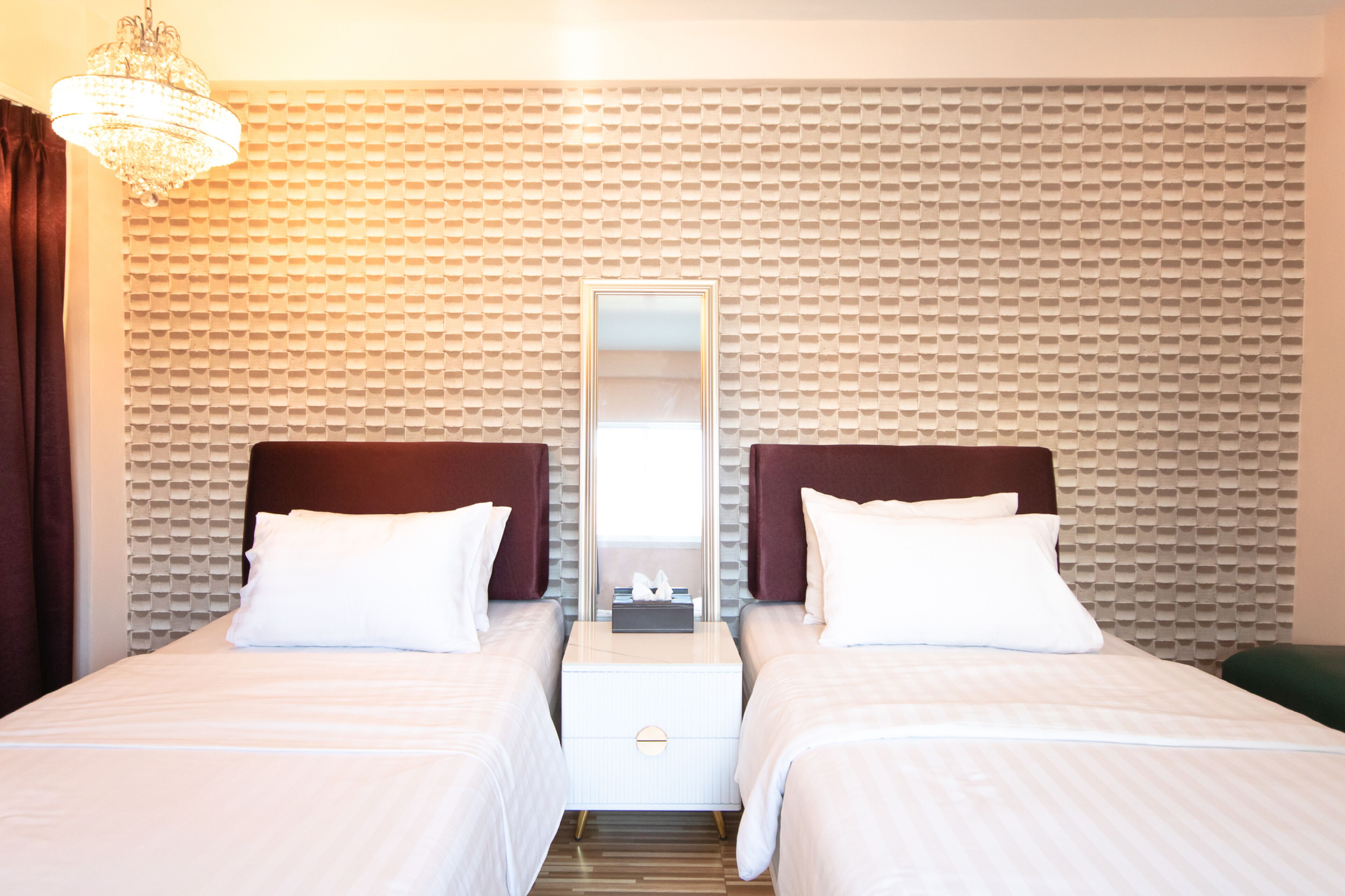 Habitación de hotel con dos camas, un espejo grande, una araña y una pared con textura.
