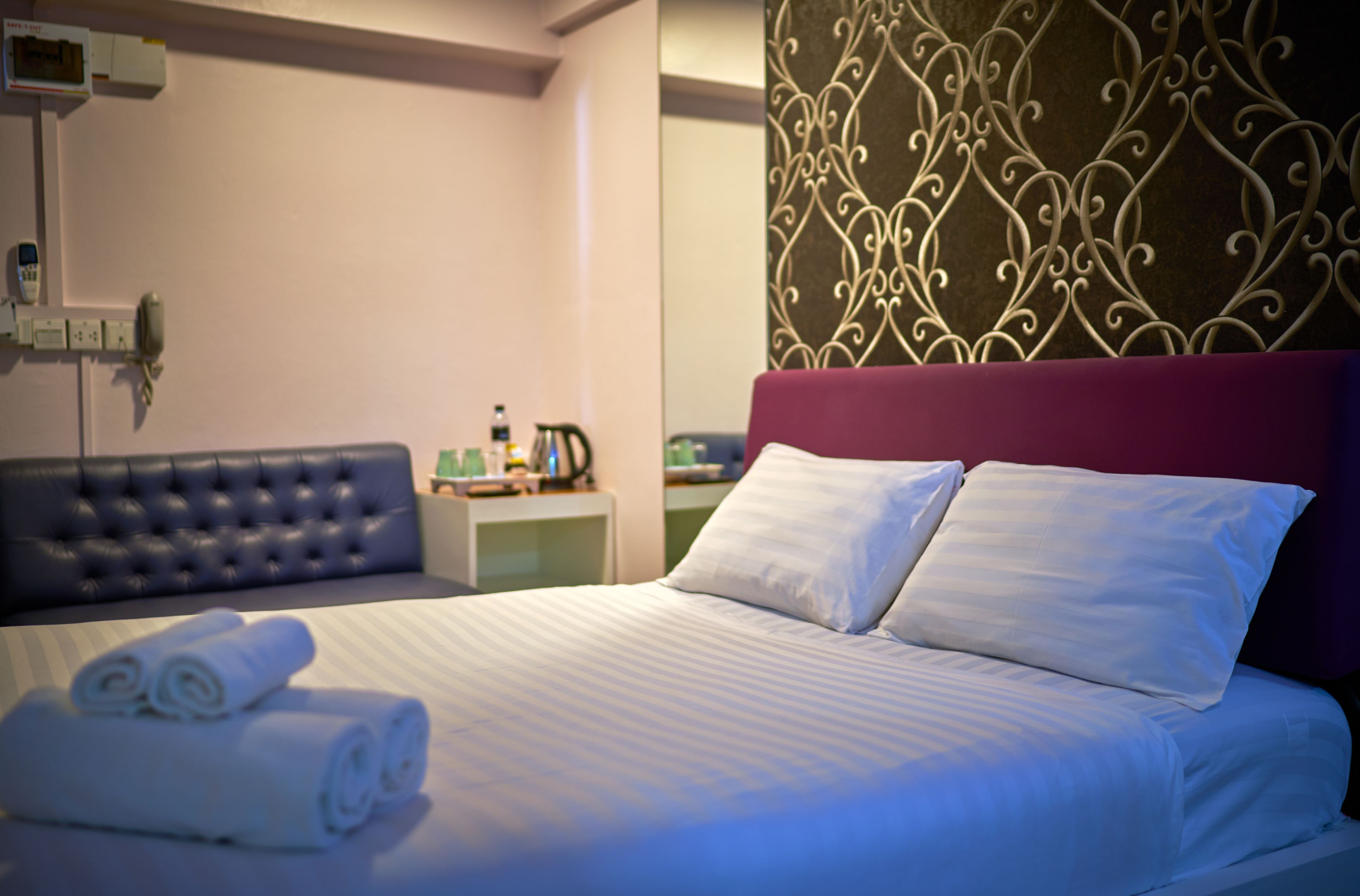A neatly made bed with white linens, a purple headboard, and a decorative wall panel.