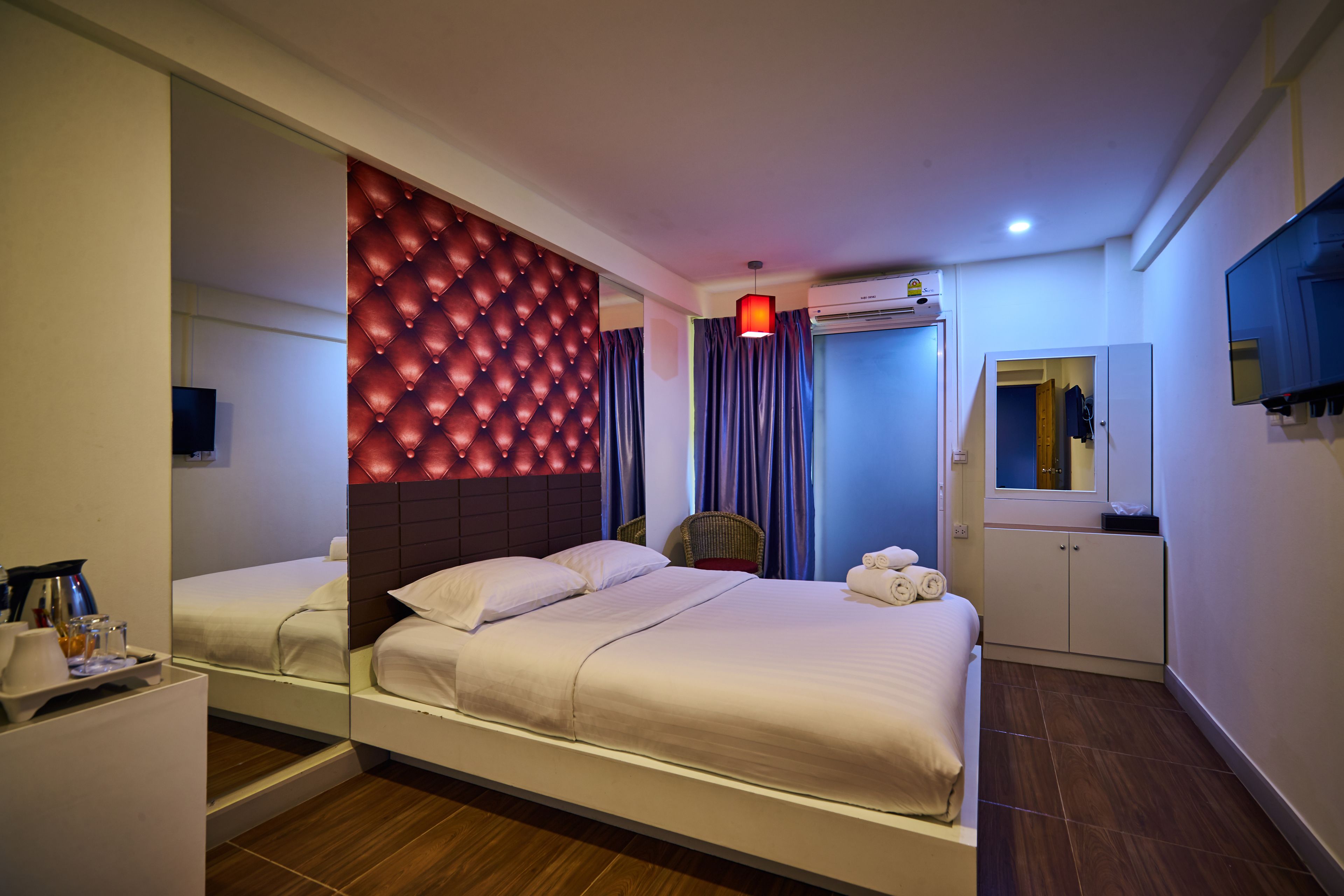 A modern hotel room with a large bed, a mirror, a wardrobe, and a television.