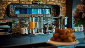 Una barra de desayuno con un fondo de pared de piedra, una máquina de café, un tostador y un cuenco de frutas.
