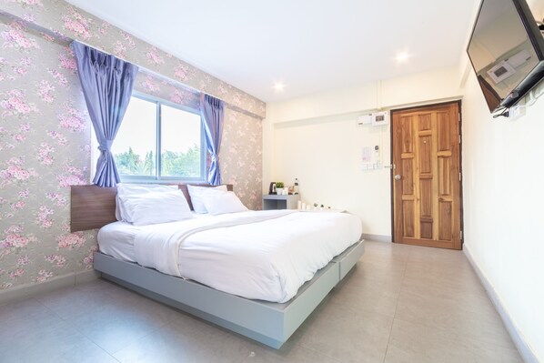 A bedroom with a bed, curtains, a window, a wooden door, and a TV mounted on the wall. - Sweetloft Hotel Don Muang (Bangkok)